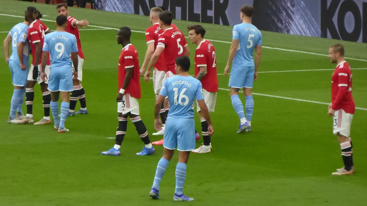Jogadores do Manchester United em vermelho e do Manchester City em azul reunidos na área