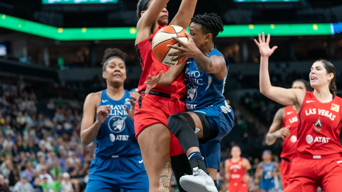 Jogadora do Minnesota Lynx avança com a bola entre atletas de uniformes azuis e vermelhos sob a cesta.
