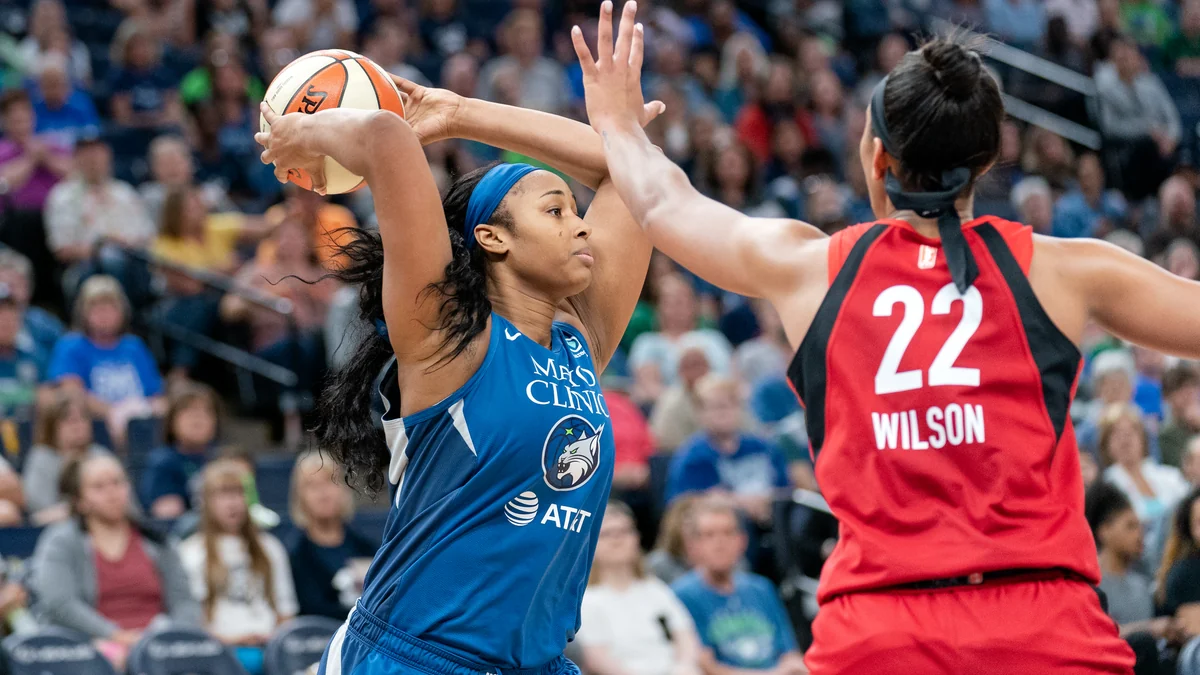 Jogadora do Minnesota Lynx protege a bola acima da cabeça diante da marcação de A’ja Wilson, número 22 das Aces.