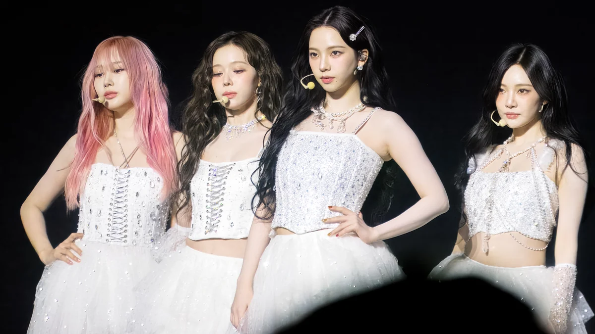 The four aespa members onstage in white outfits with headset microphones.