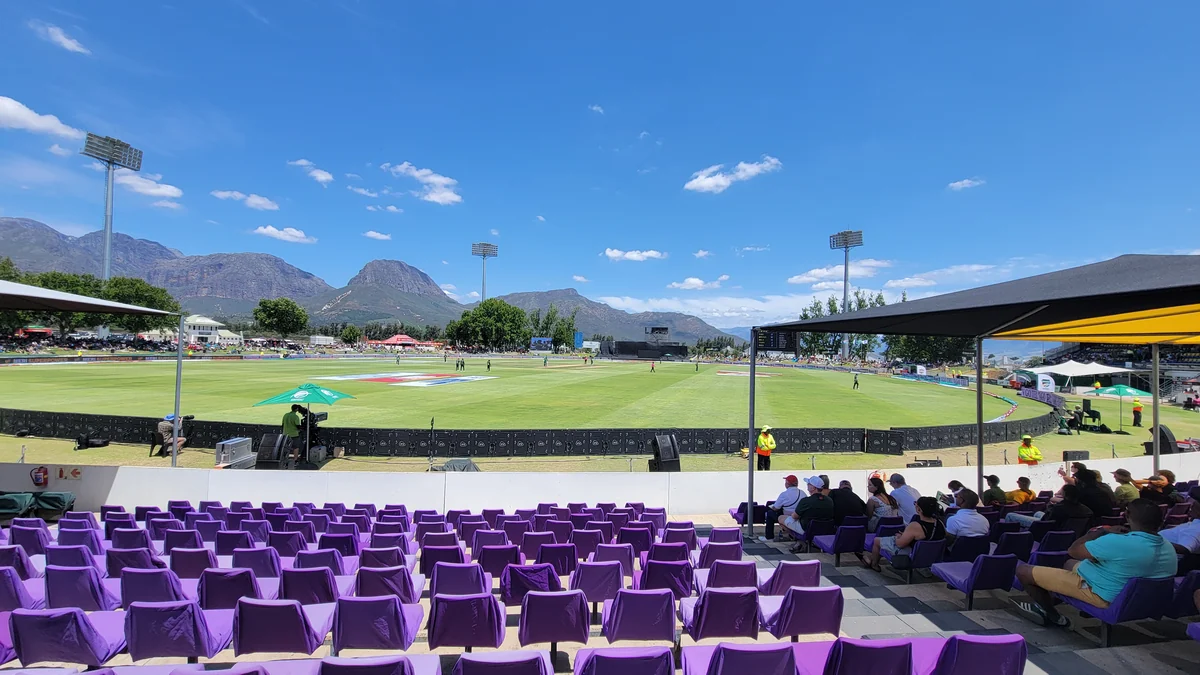 Terrain de cricket avec sièges violets et montagnes sous un ciel bleu