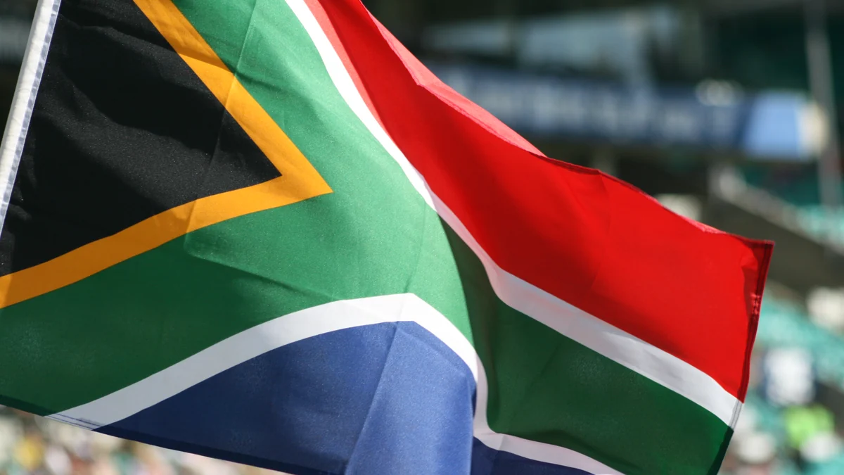 Bandeira da África do Sul em primeiro plano, com arquibancadas desfocadas ao fundo.