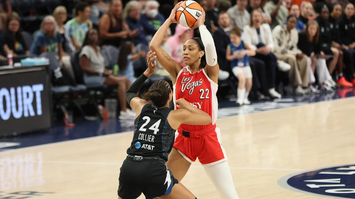 A’ja Wilson, wearing a red Las Vegas Aces uniform, holds the ball overhead in front of Napheesa Collier.
