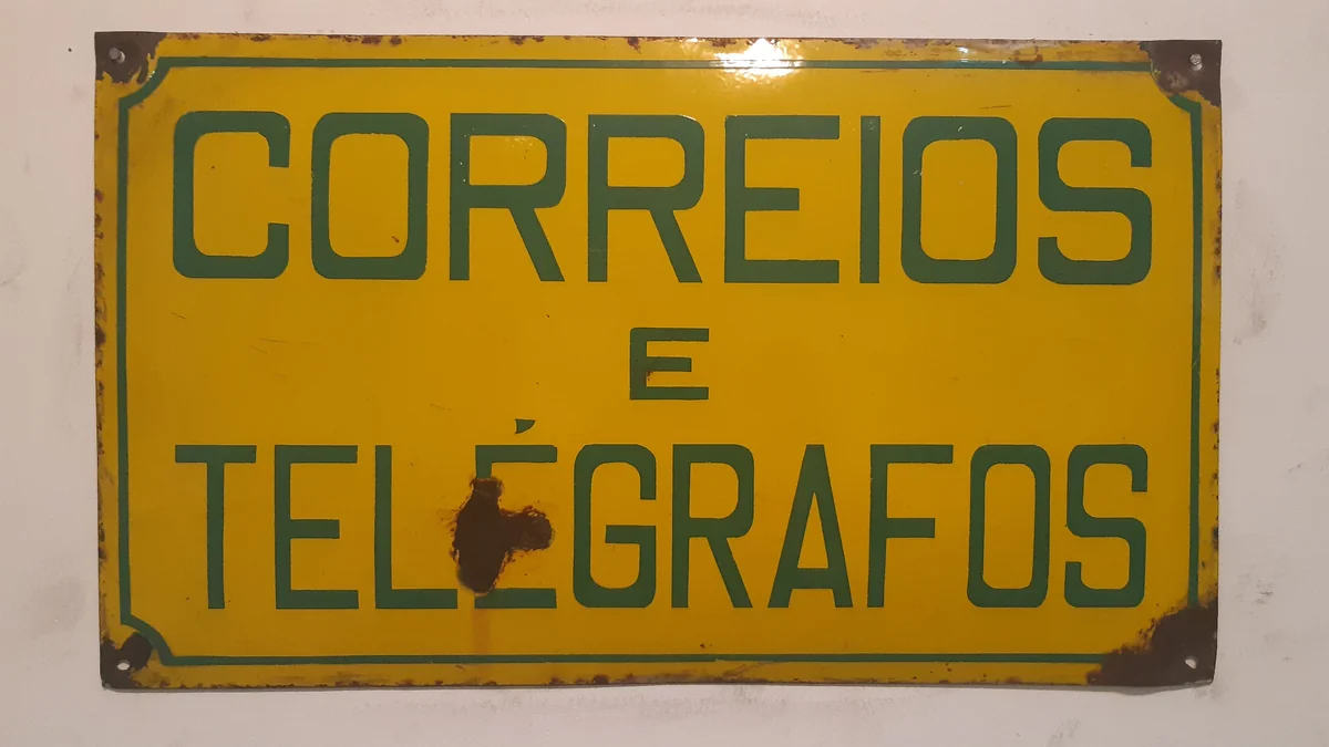 Placa antiga amarela e verde com a inscrição Correios e Telégrafos