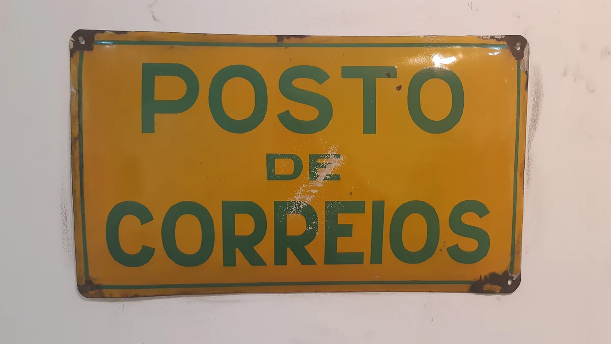 Placa antiga amarela e verde com as palavras Posto de Correios