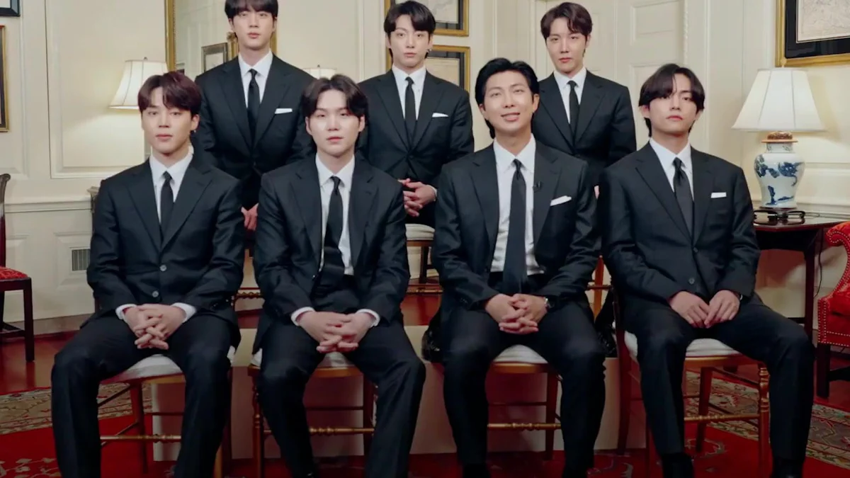 Los siete integrantes de BTS posan sentados y de pie con trajes negros en una sala.