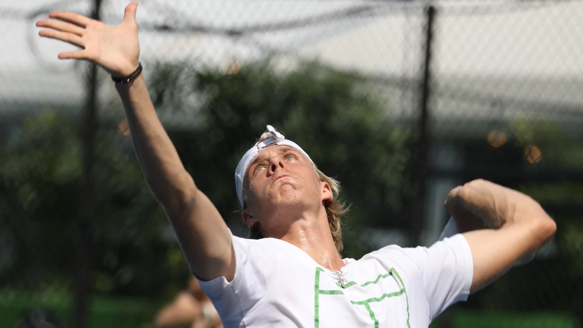 Denis Shapovalov lance la balle pour servir, vêtu d’un maillot blanc et d’une casquette retournée.