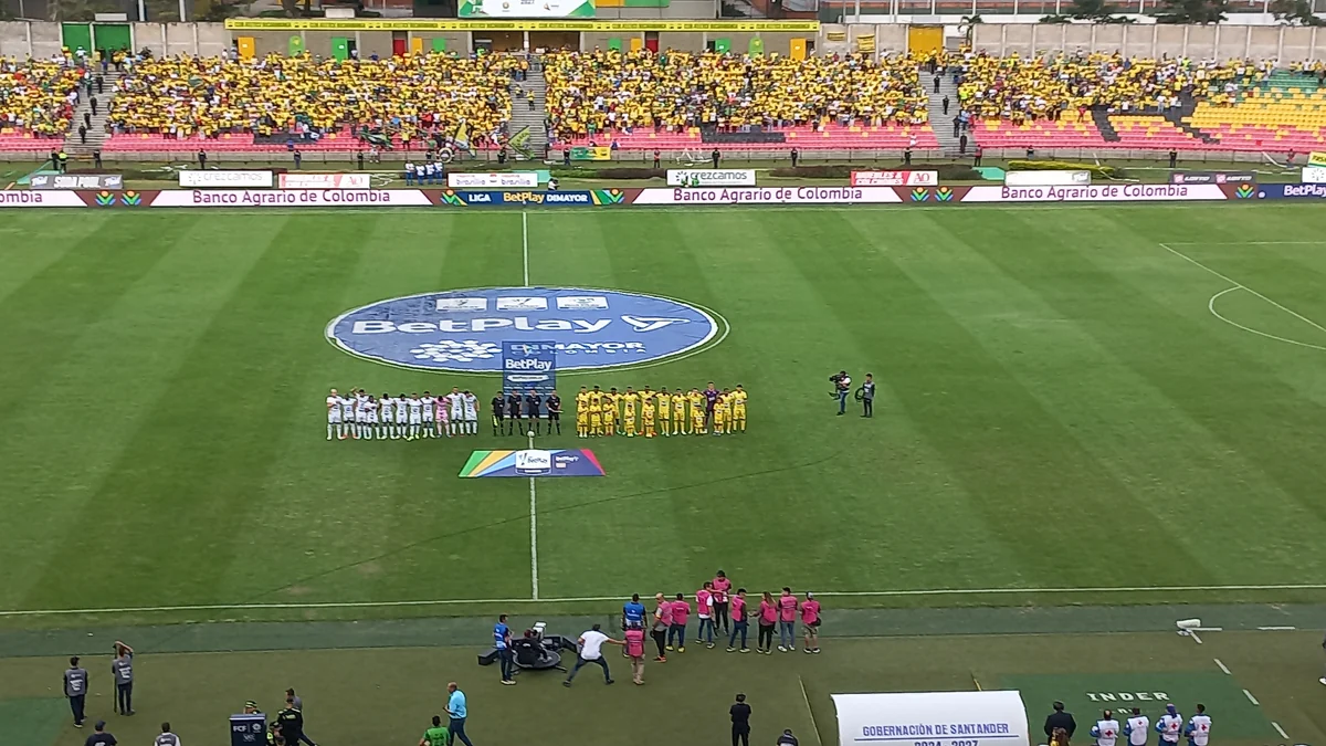 Teams lined up at midfield in front of a stand filled with supporters in yellow