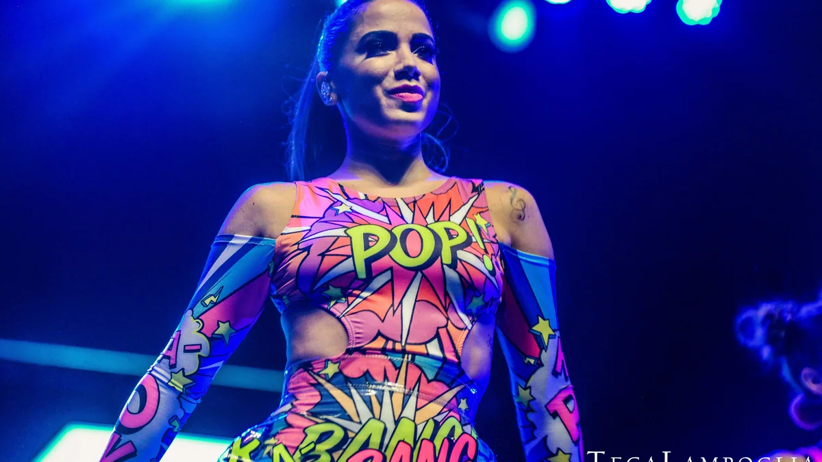 Anitta singing during a live performance on a lit stage.