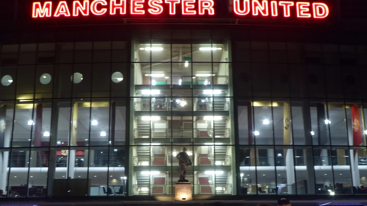 Fachada envidraçada de Old Trafford à noite, sob o letreiro luminoso Manchester United