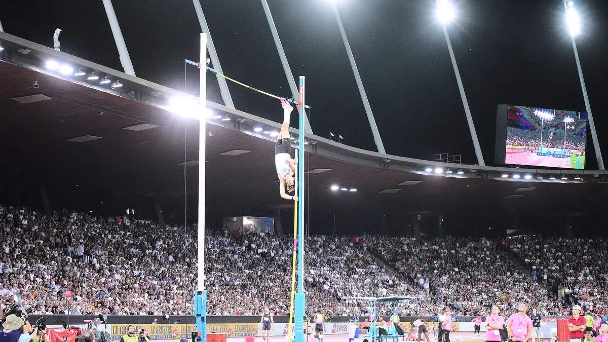 Saltador con pértiga invertido sobre el listón en un estadio lleno de noche