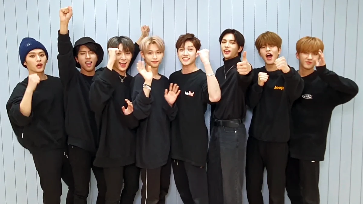 Ocho integrantes de Stray Kids vestidos de negro, con los brazos levantados y gestos de celebración