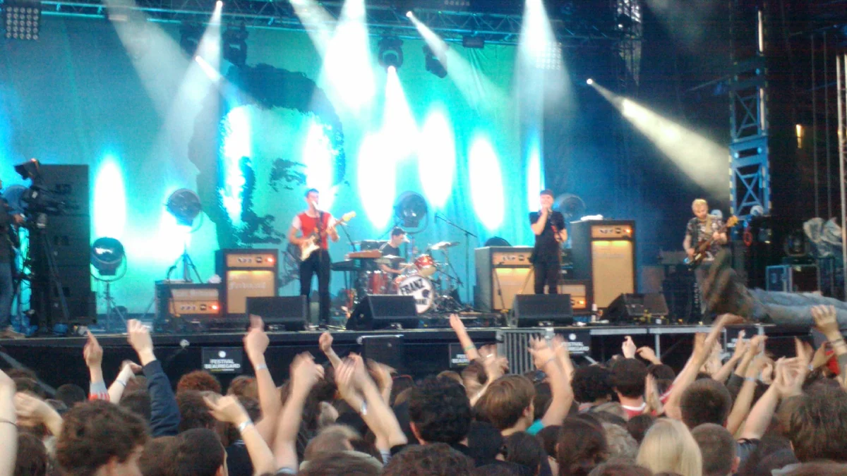 Band performing under blue lights before an audience with raised arms