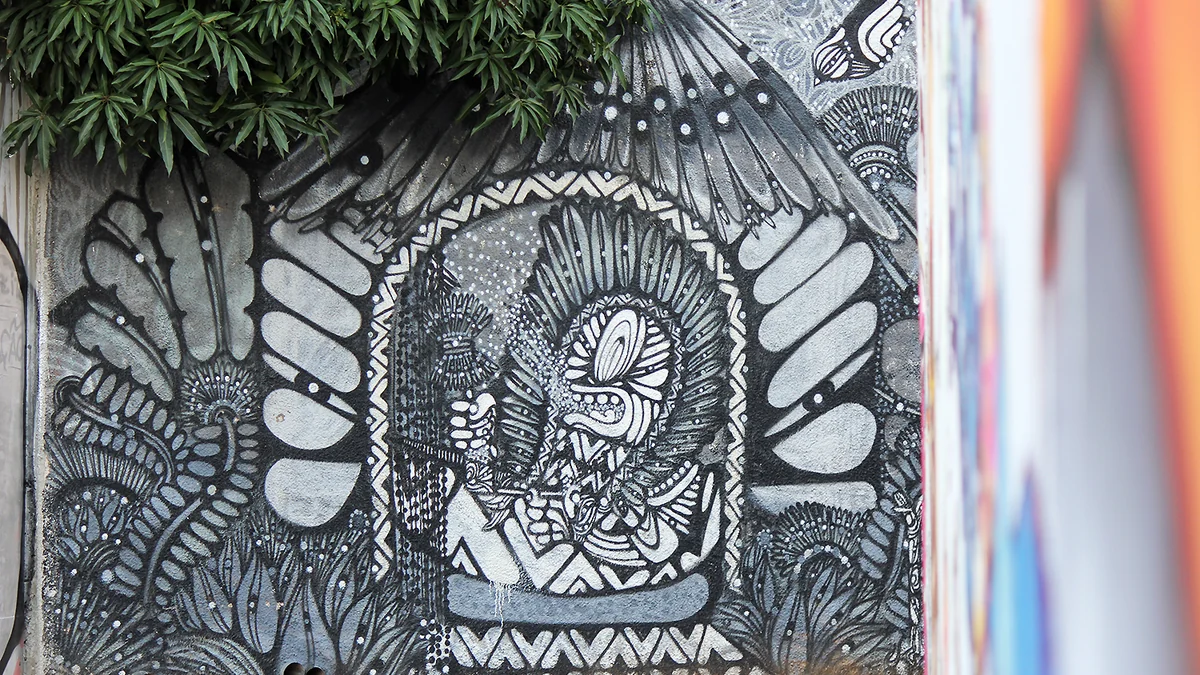 Mural detallado en negro, blanco y gris parcialmente cubierto por hojas