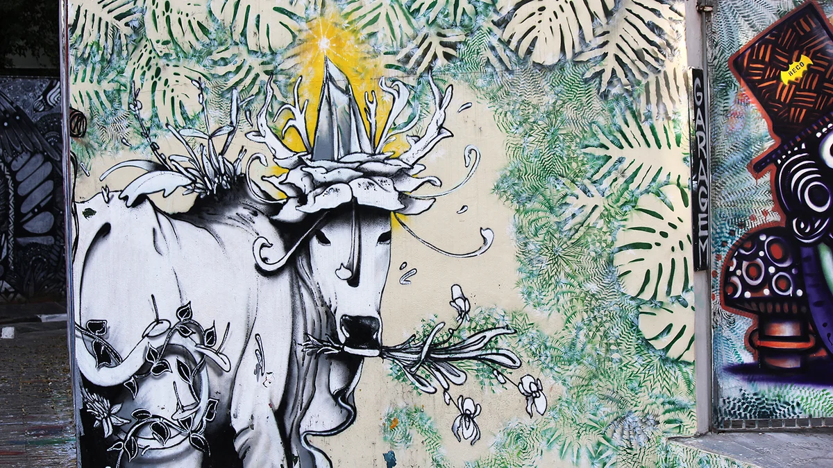 Mural con una figura alargada en blanco y negro, hojas verdes y detalles amarillos
