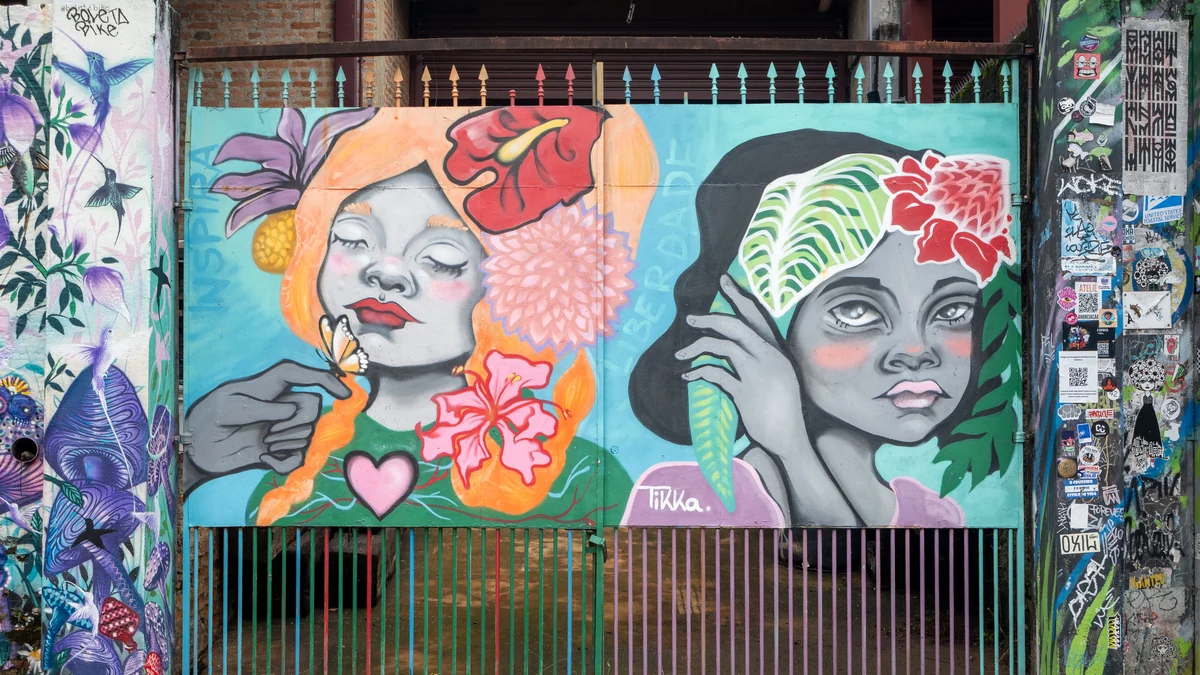 Fresque de deux visages féminins avec des fleurs et des feuilles au-dessus d’un portail grillagé