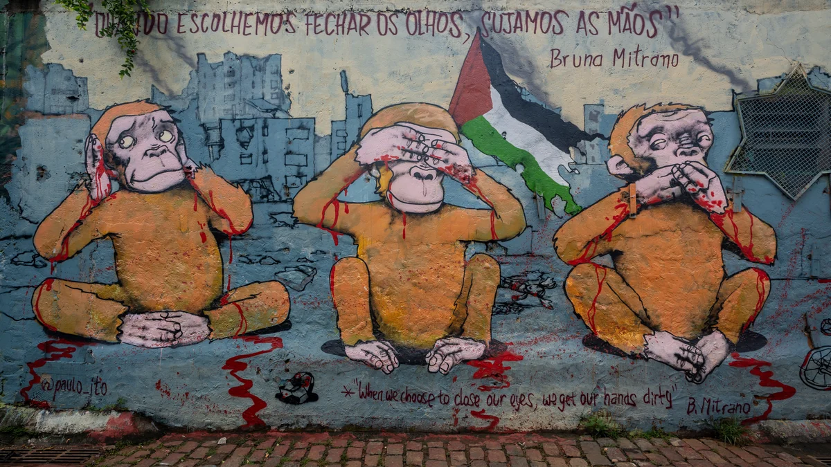Fresque de trois singes se couvrant les oreilles, les yeux et la bouche devant des immeubles et un drapeau palestinien