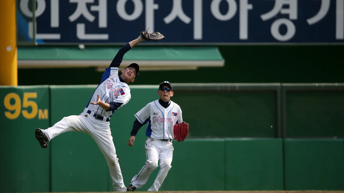 A Mongolia player leaps with his glove raised as a teammate follows the play in the outfield.