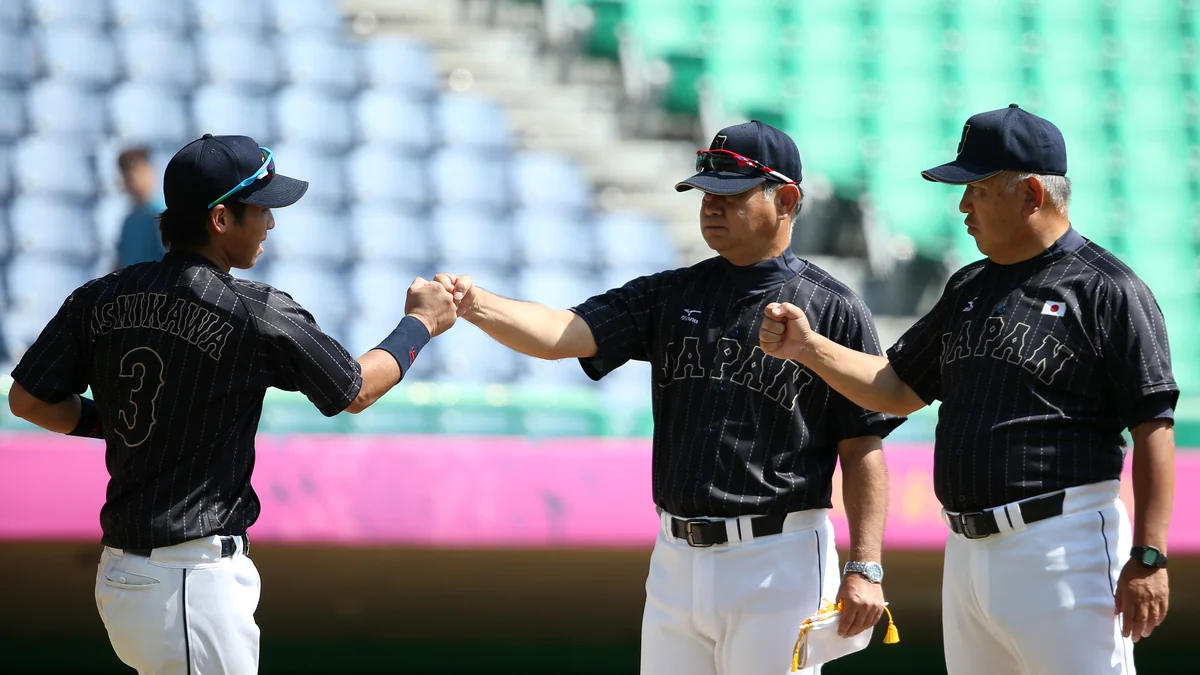 Three members of Japan’s baseball team in black uniforms exchange fist bumps on the field.