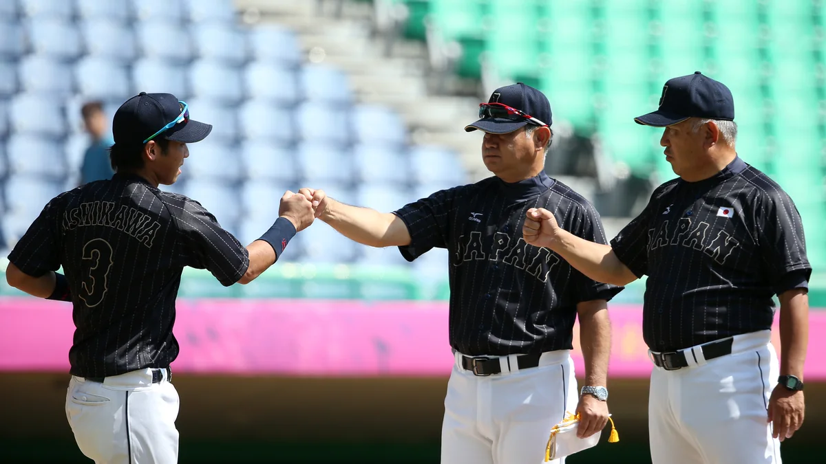 Três integrantes da equipe japonesa de beisebol, de uniforme preto, trocam cumprimentos no campo.