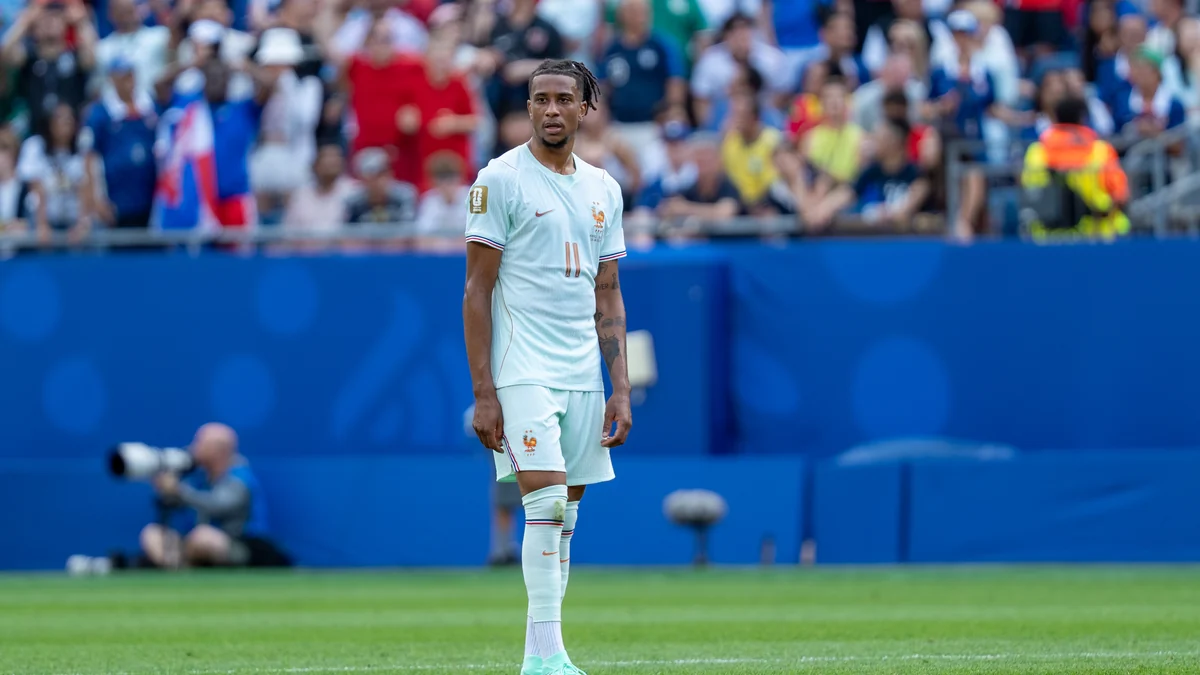 Michael Olise em pé no campo com o uniforme branco da seleção francesa