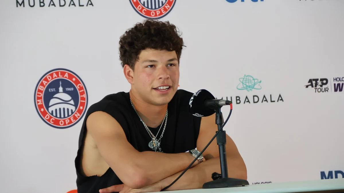 Ben Shelton, con una camiseta negra sin mangas, habla ante un micrófono en una rueda de prensa.