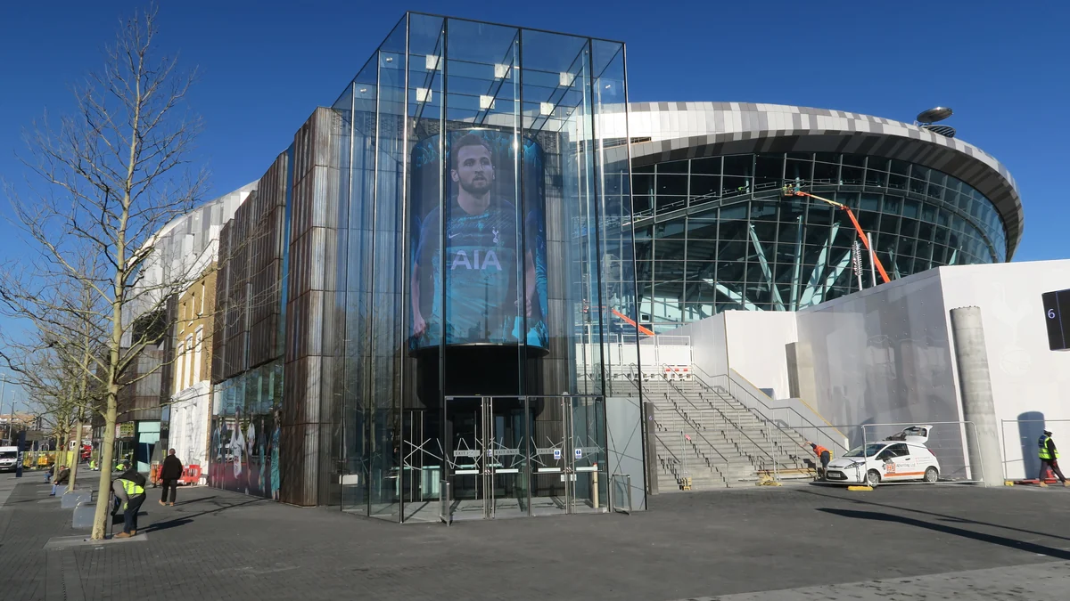 Glass-fronted entrance and staircase outside Tottenham Hotspur Stadium under a blue sky