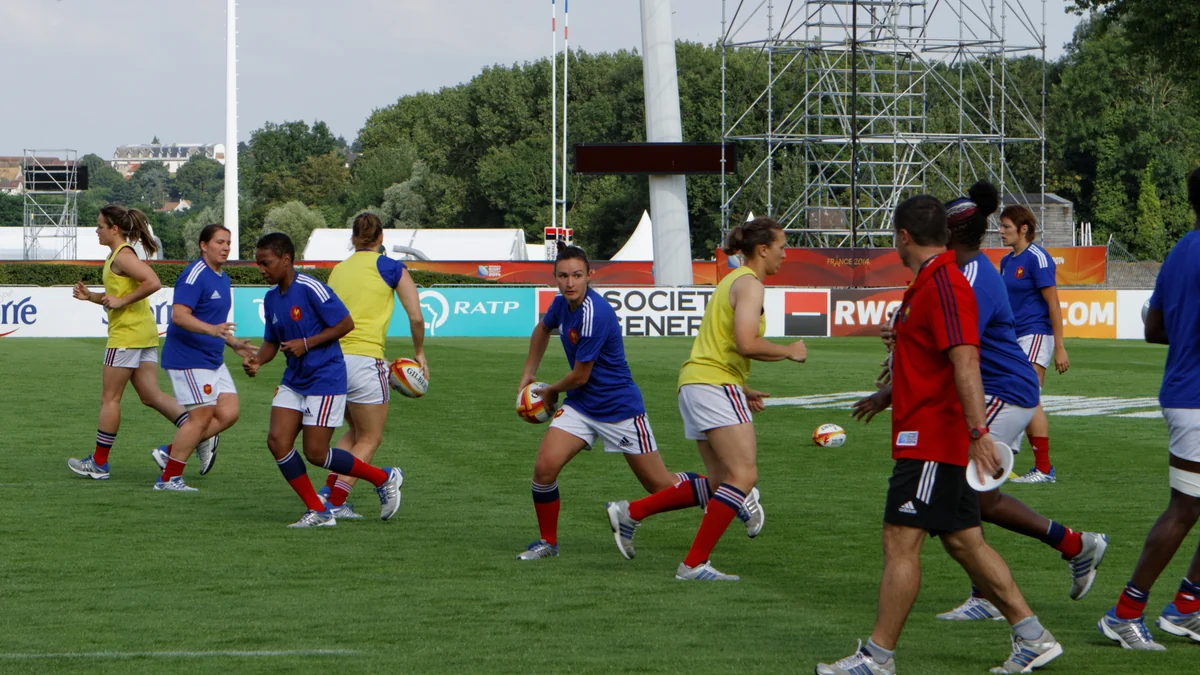 Des joueuses de rugby françaises s’entraînent avec des ballons et des chasubles jaunes sur un terrain.