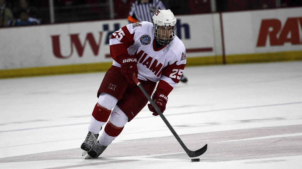 Blake Coleman patina con el disco con el uniforme blanco y rojo de Miami University.