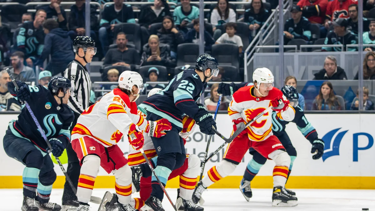 Blake Coleman, de blanco y rojo, disputa el disco entre jugadores de los Flames y el Seattle Kraken.