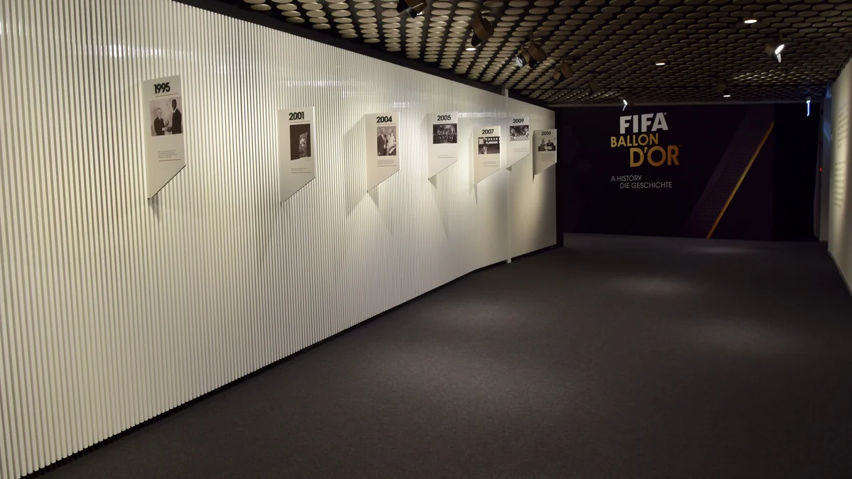 Corredor de museu com painéis cronológicos e letreiro FIFA Ballon d’Or ao fundo