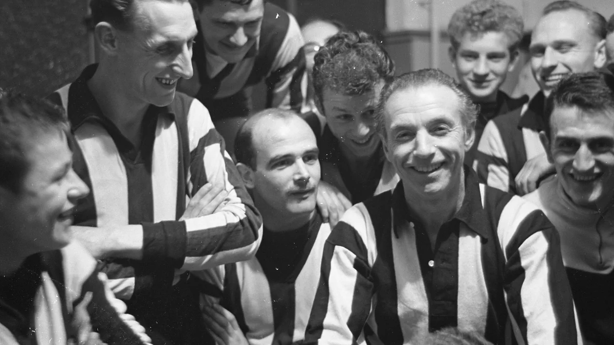 Stanley Matthews smiles while surrounded by football players in striped shirts