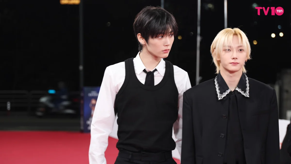 Two BOYNEXTDOOR members wearing black outfits on a red carpet