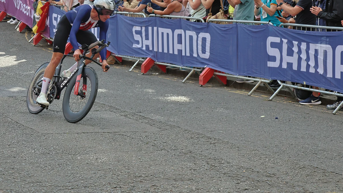 Brandon McNulty leans his bicycle through a corner during a time trial beside barriers and spectators