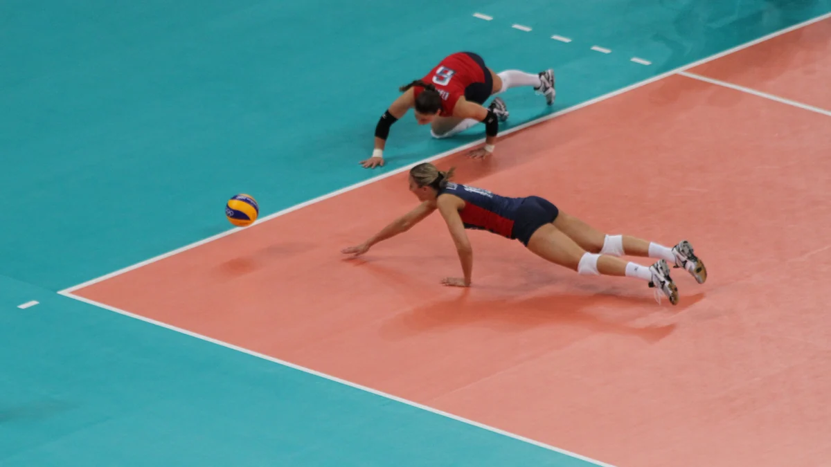 Duas jogadoras de voleibol se lançam ao chão em direção à bola perto da linha lateral.