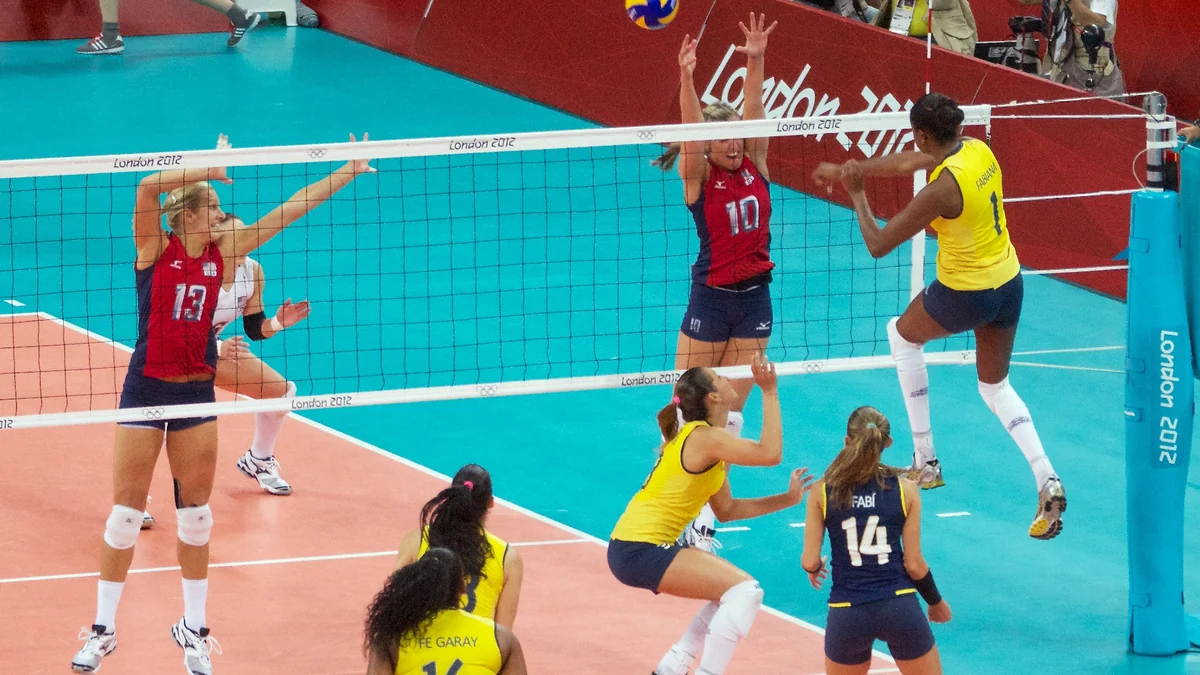 Atacante do Brasil, de amarelo, salta diante do bloqueio de duas jogadoras dos Estados Unidos.