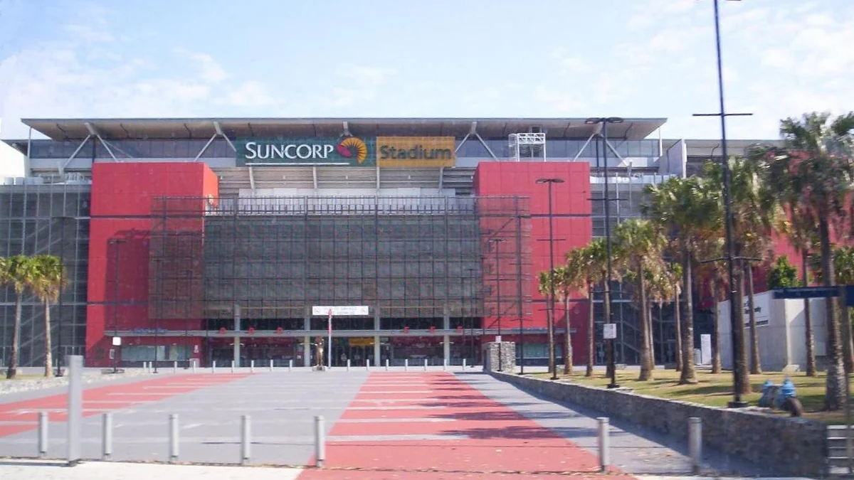 Fachada do Suncorp Stadium com painéis vermelhos, palmeiras e uma praça de acesso