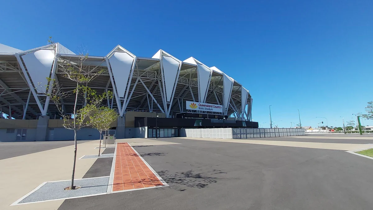 Área externa do Queensland Country Bank Stadium sob céu azul, com fachada branca e acesso pavimentado