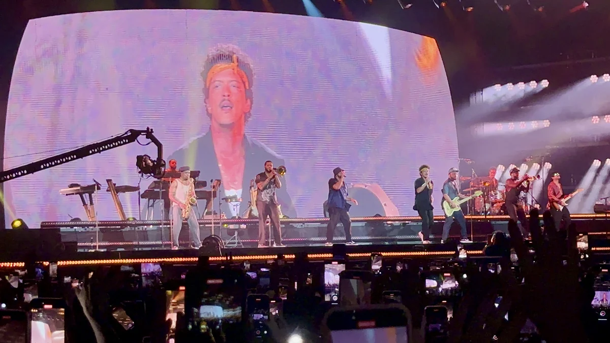 Bruno Mars y músicos en el escenario ante una pantalla y teléfonos levantados entre el público