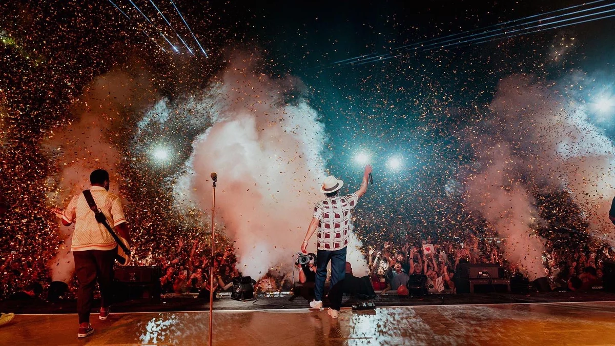 Bruno Mars de espaldas en el escenario con su banda, humo y confeti ante el público