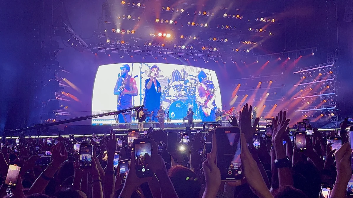 Escenario iluminado de Bruno Mars visto detrás de un público con teléfonos levantados