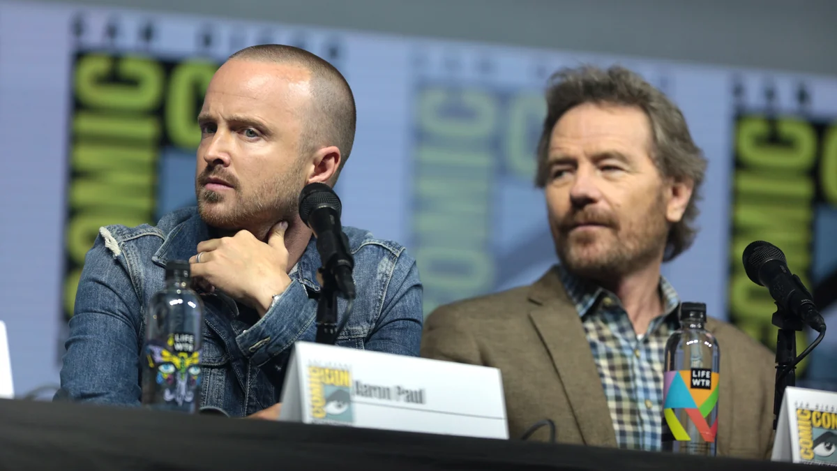Aaron Paul and Bryan Cranston seated at microphones during a Comic-Con panel