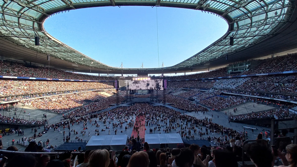 Vue générale d’un stade rempli, avec scène centrale et public pendant un concert