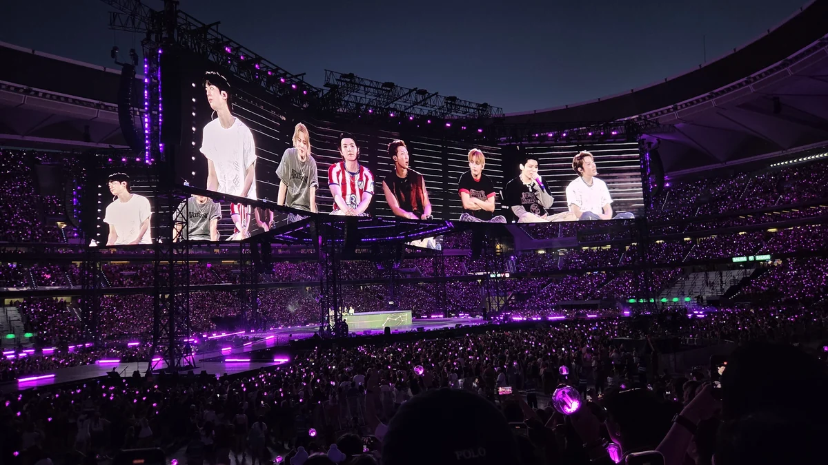 Un écran géant montre les sept membres de BTS dans un stade éclairé en violet