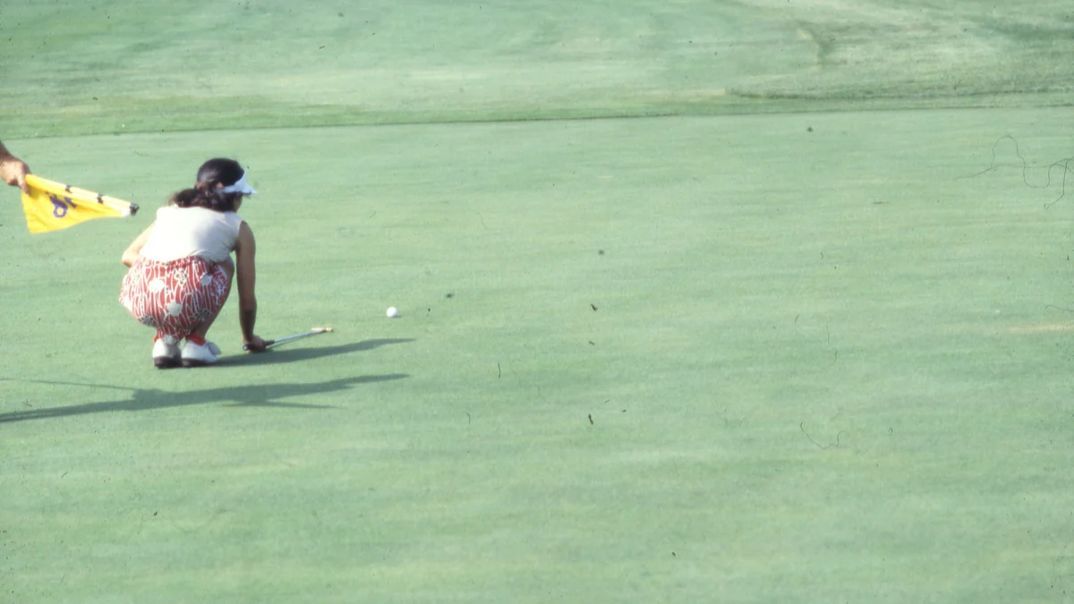 Golfista vista de espaldas agachada junto a la bola y el palo sobre el green