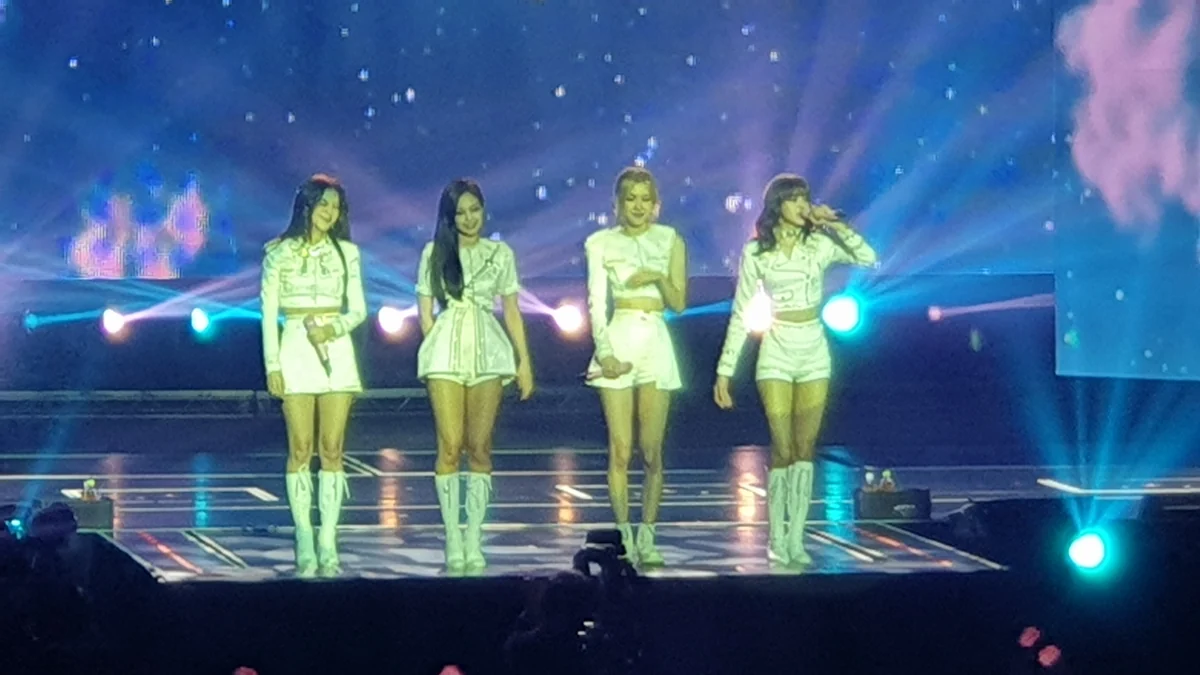 Four BLACKPINK members in white outfits standing side by side onstage