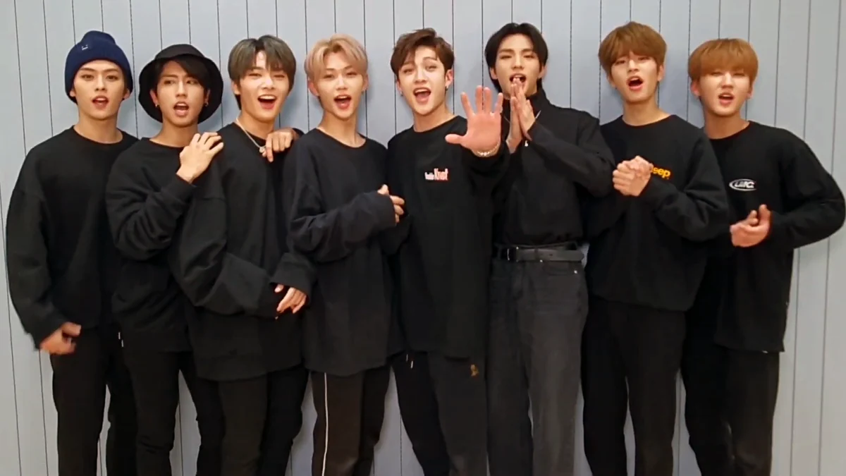 Ocho integrantes de Stray Kids vestidos de negro ante una pared gris
