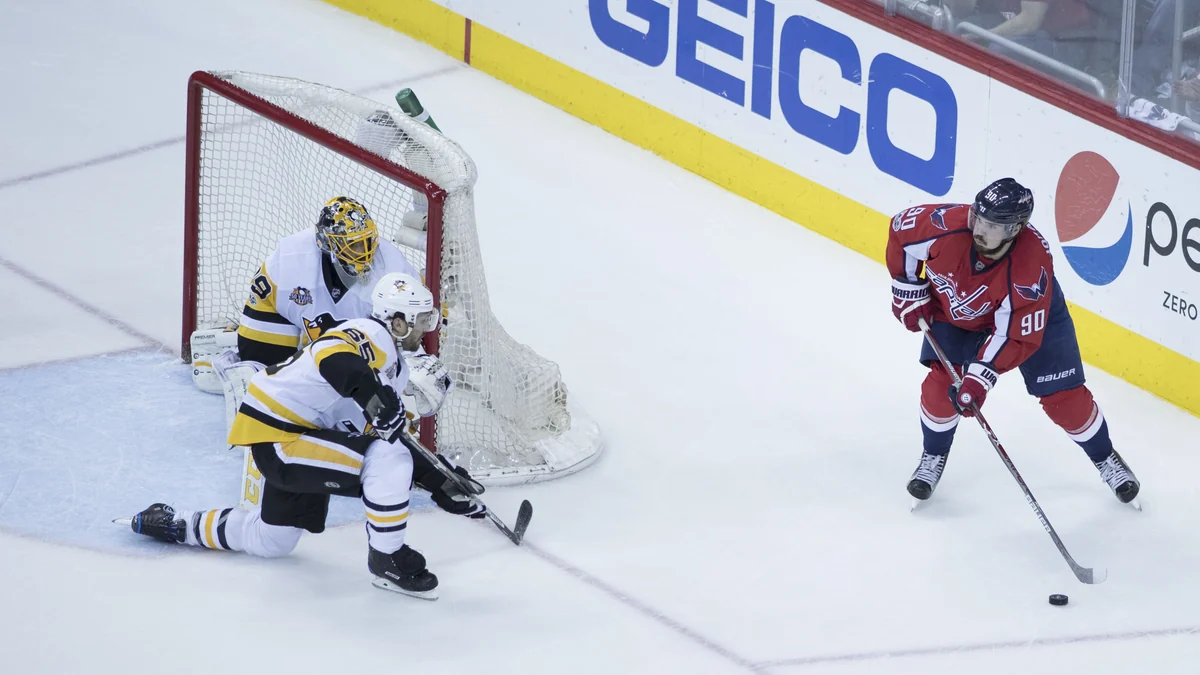 Un joueur des Capitals contrôle le palet devant deux défenseurs et le gardien des Penguins