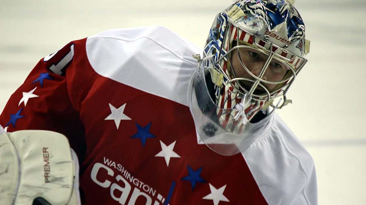 El portero de Washington Capitals Philipp Grubauer se agacha sobre el hielo con camiseta roja y máscara