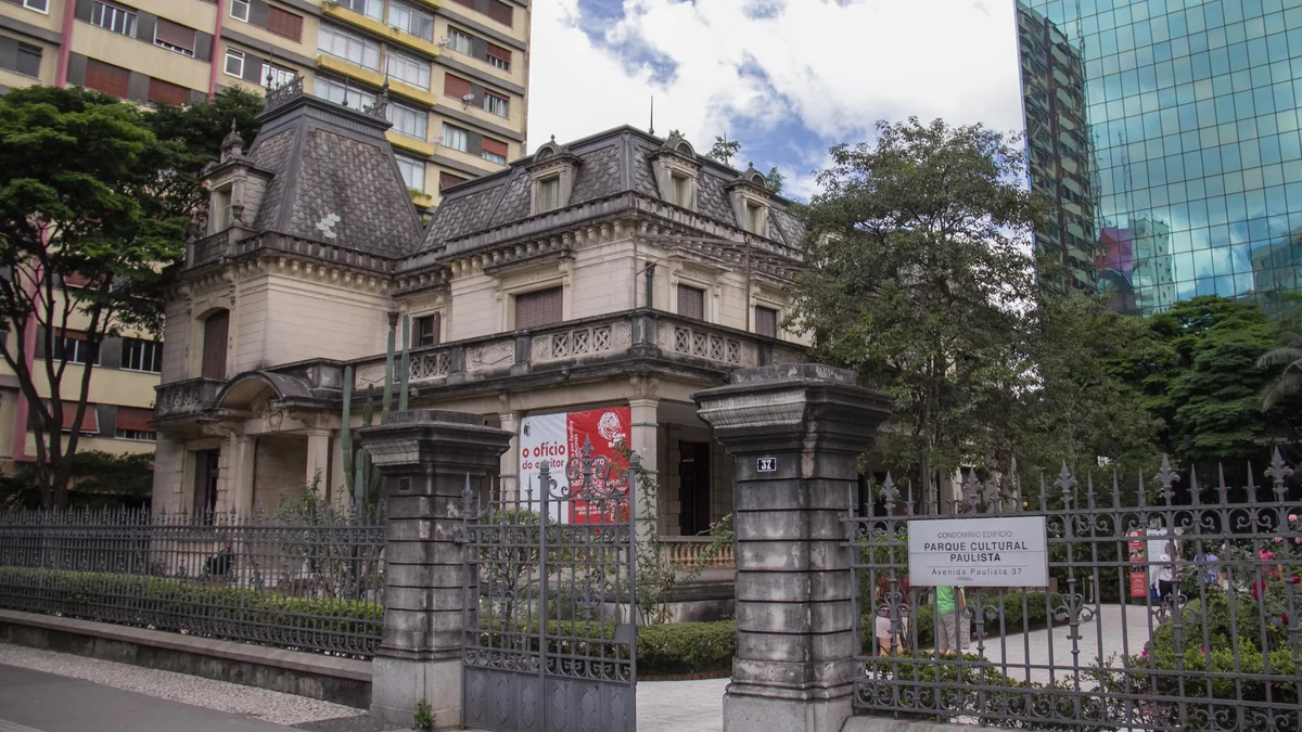Fachada da Casa das Rosas vista atrás do gradil e do jardim na Avenida Paulista
